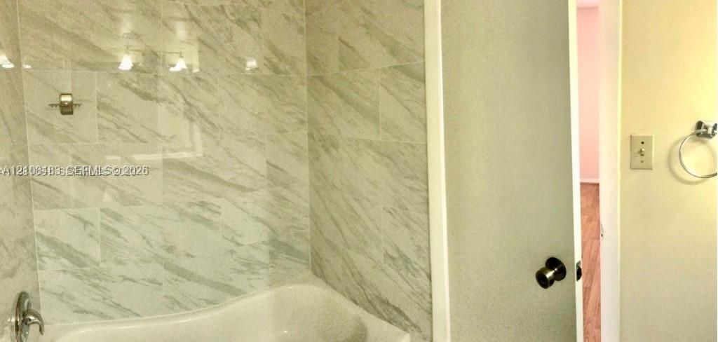 Full-height wall tiling with a vein-patterned finish, built-in bathtub, brushed metallic faucet, and wall-mounted circular towel ring