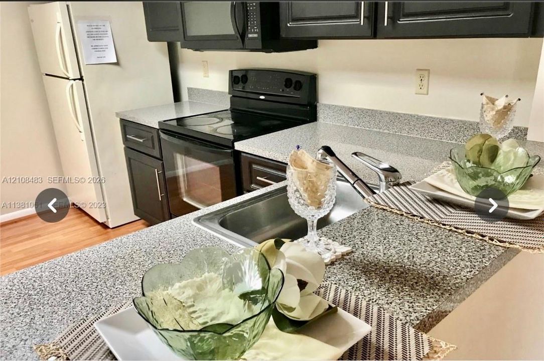 Kitchen featuring dark cabinetry, speckled stone-finish countertops, stainless steel sink with a high-arch faucet, and black appliances including an electric range and microwave