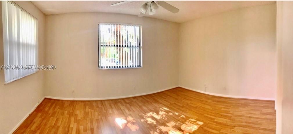 Interior room featuring wood-finish flooring, two windows with vertical blinds, and a ceiling-mounted light fixture with fan