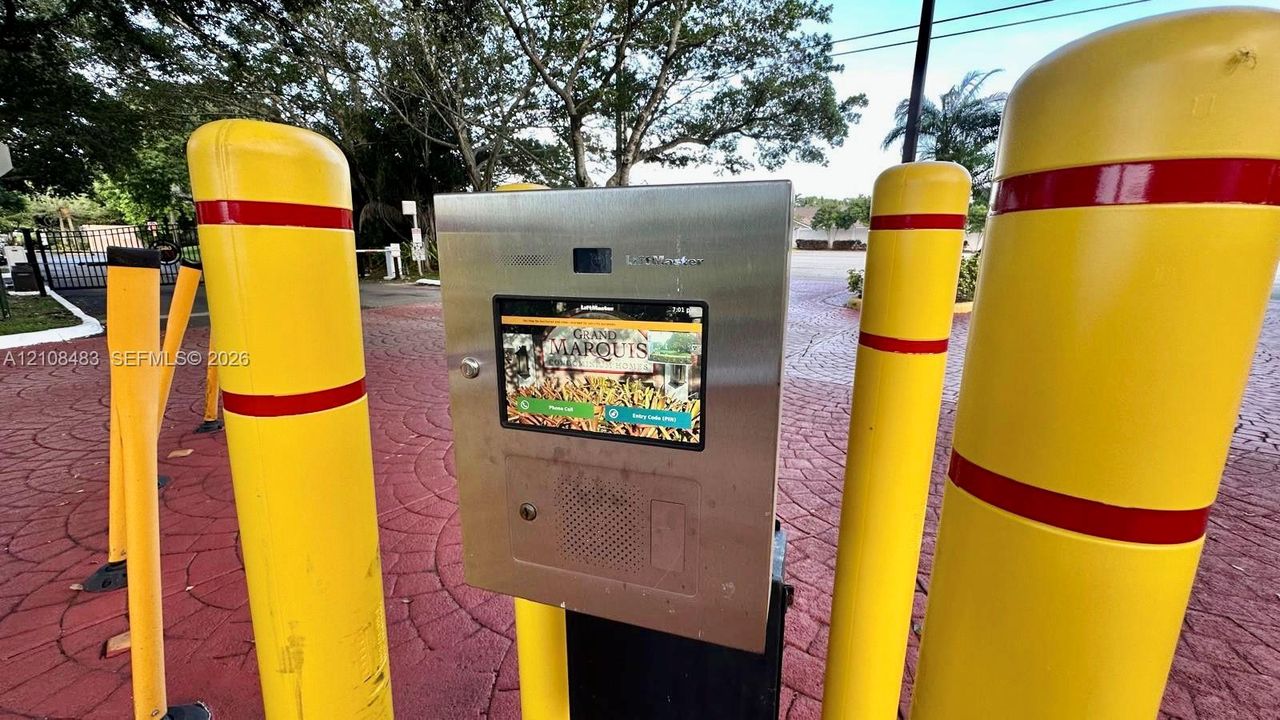 Electronic gated entry system with stainless steel housing, integrated digital touchscreen interface, and protective yellow bollards