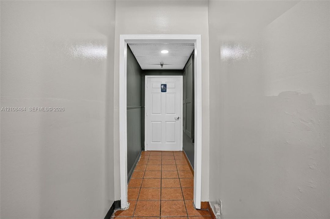 Hallway featuring ceramic tile flooring, neutral wall paint, and a six-panel door with metallic hardware