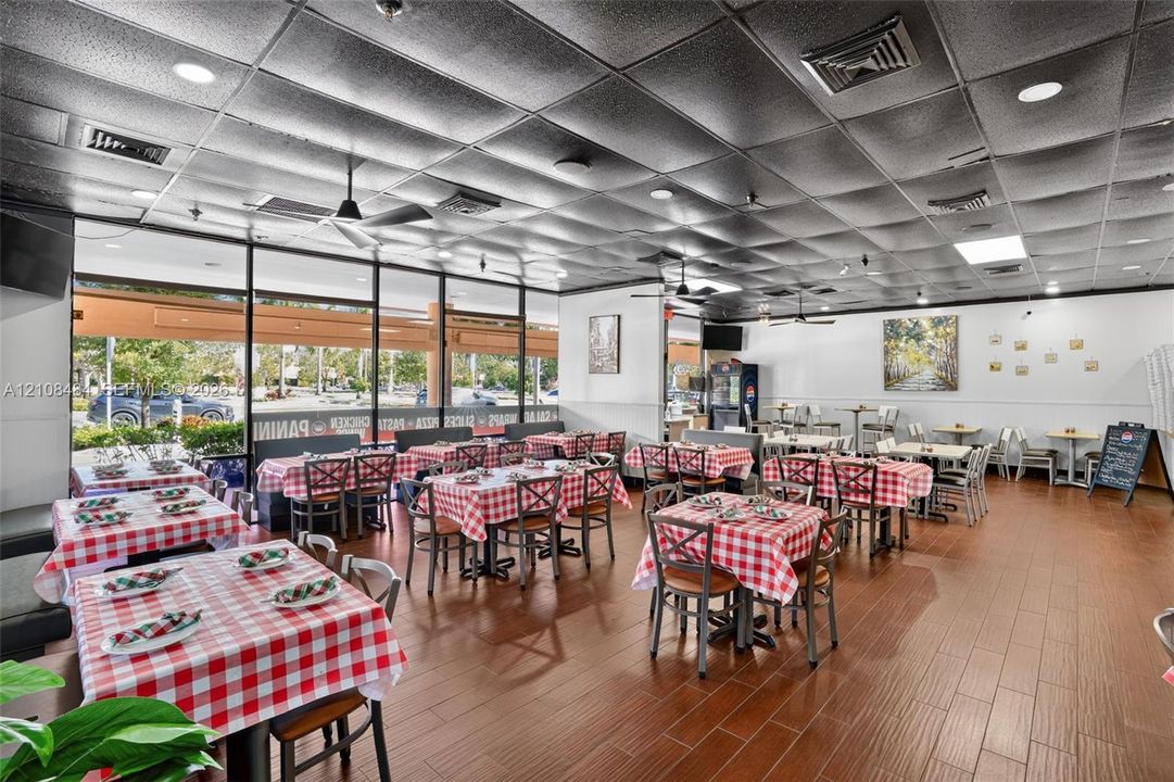 Spacious interior featuring wood-finish flooring, high-contrast ceiling tiles, recessed lighting, and extensive floor-to-ceiling glass storefront windows