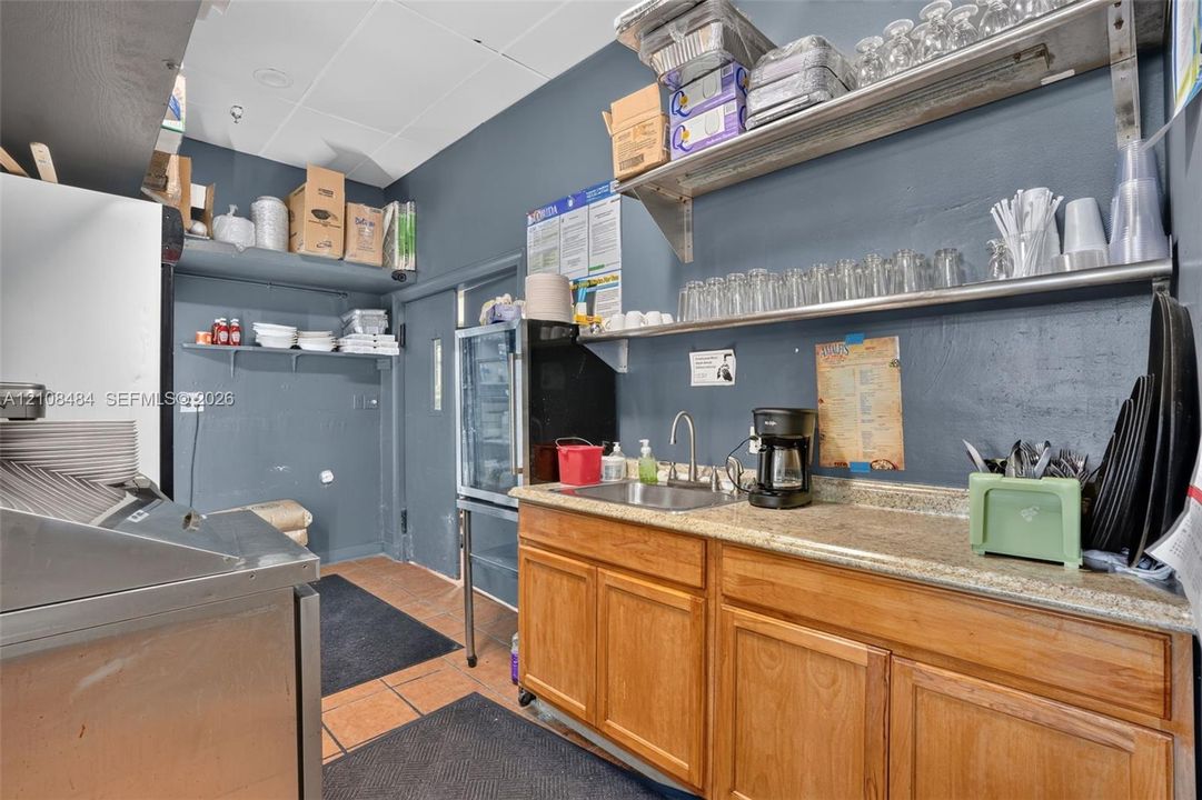 Service area featuring wood-finish cabinetry, stone-composite countertop, stainless steel sink, and tiered metal wall shelving