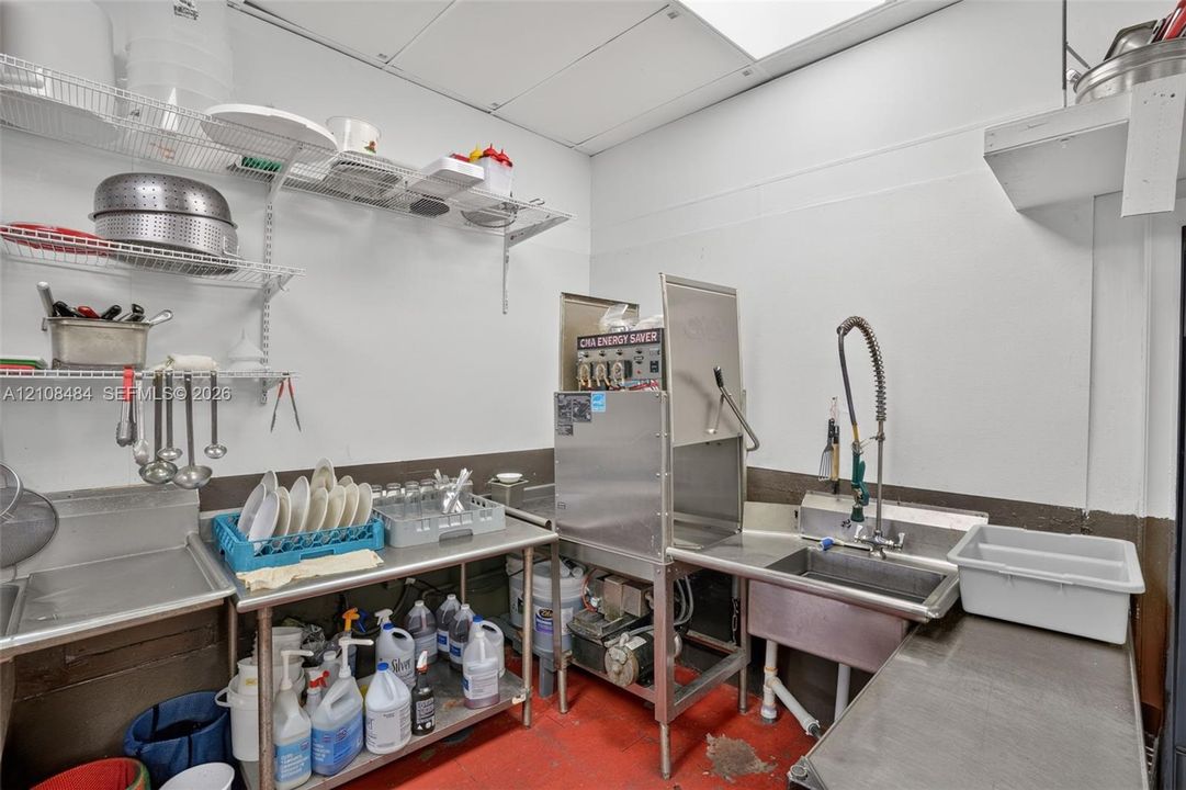 Commercial dishwashing station featuring stainless steel utility tables, a high-temperature industrial dishwasher, an integrated stainless steel sink with a commercial-grade pre-rinse faucet, and wall-mounted wire shelving