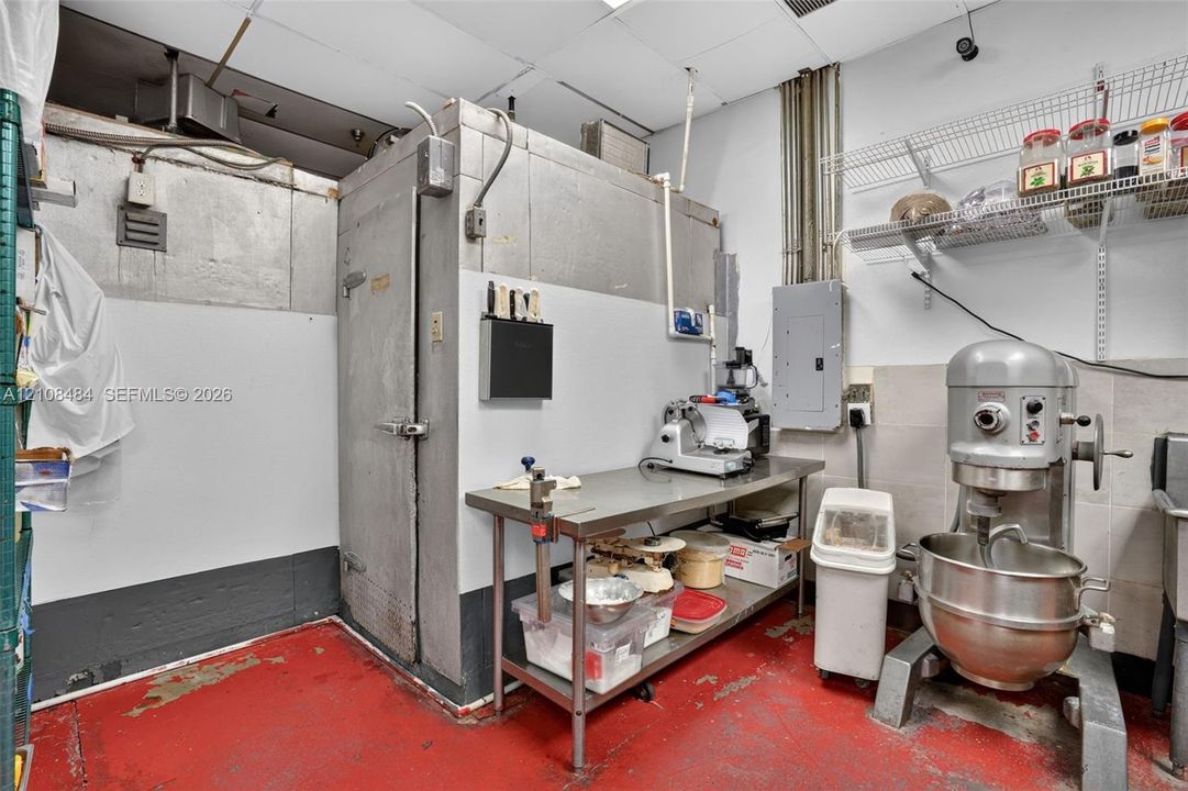 Commercial kitchen space featuring a built-in walk-in cooler, industrial-grade stainless steel prep table, and mounted wire shelving