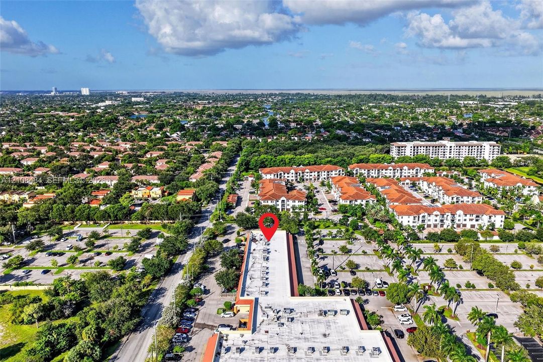 Aerial perspective featuring a flat-roof commercial structure, expansive asphalt parking surfaces, and established palm tree landscaping