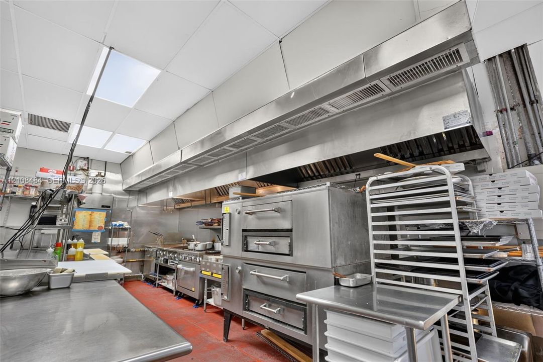 Commercial kitchen equipped with a multi-level deck oven, stainless steel food preparation surfaces, and an overhead stainless steel ventilation hood system