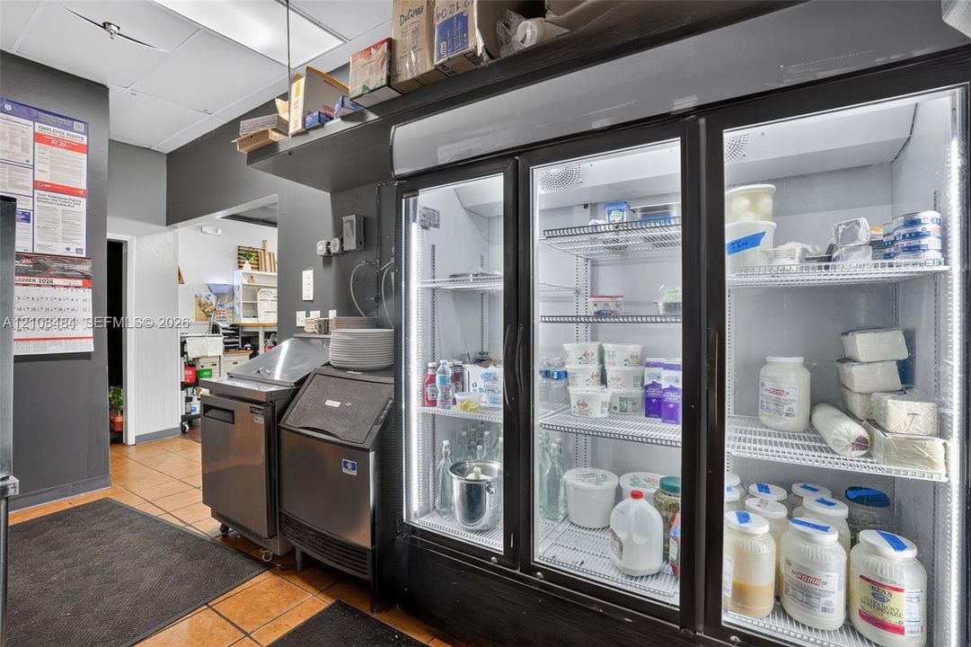 Commercial kitchen featuring a multi-section glass-door refrigeration unit, stainless steel ice machine, and tile flooring