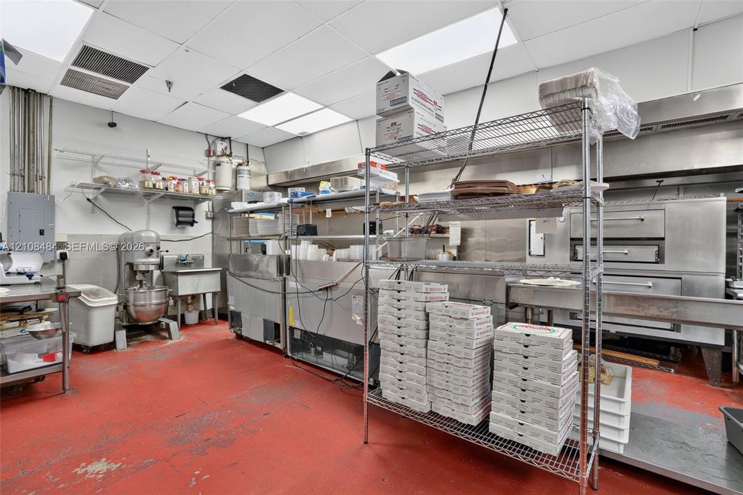 Commercial kitchen space featuring stainless steel food preparation surfaces, commercial-grade oven equipment, stainless steel sink basin, drop ceiling, and high-durability floor coating