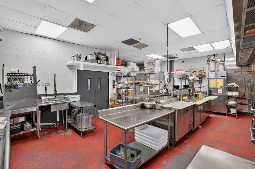 Commercial-grade kitchen featuring stainless steel prep tables, a multi-compartment sink, an integrated ventilation hood system, and industrial flooring
