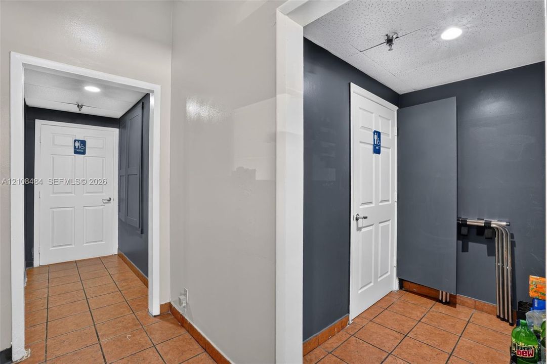 Hallway featuring terracotta-toned tile flooring, charcoal-painted walls, and white six-panel doors with integrated signage