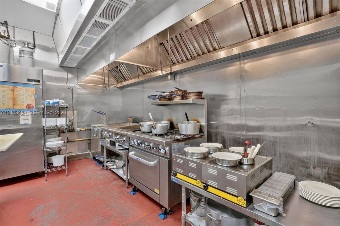 Commercial-grade kitchen featuring stainless steel wall cladding, expansive overhead ventilation system, heavy-duty gas range, and durable seamless flooring