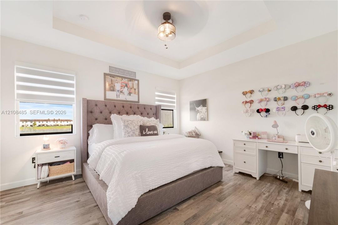 Tray ceiling with center-mounted light fixture, wood-finish flooring, and dual-layered window shades