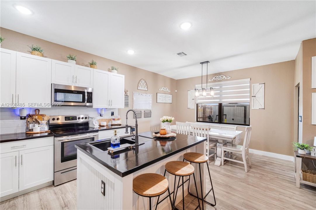 Kitchen featuring white shaker-style cabinetry, dark stone countertops, a central island with an undermount sink, stainless steel appliances, and wood-finish flooring