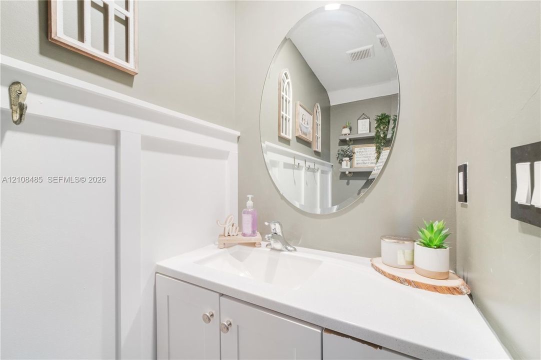 Oval wall-mounted mirror, white vanity cabinet with a integrated sink, polished chrome faucet, and board-and-batten wall detailing