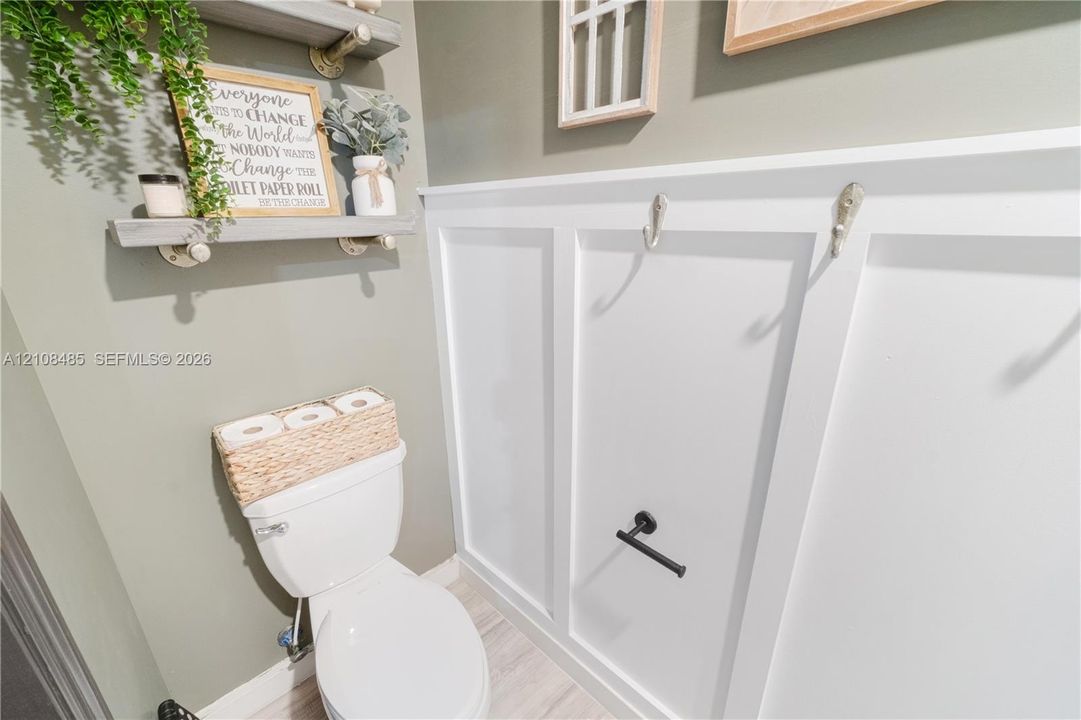 White board-and-batten wainscoting, matte black hardware, dual wall-mounted floating wood shelves, and wood-finish flooring