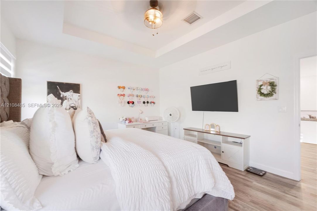 Tray ceiling featuring a central brushed-nickel ceiling fan with an integrated light fixture and wood-finish flooring