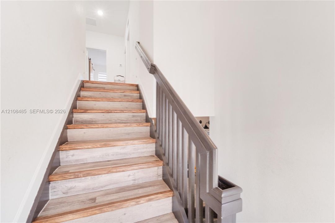 Staircase featuring wood-finish treads and a painted railing with vertical balusters