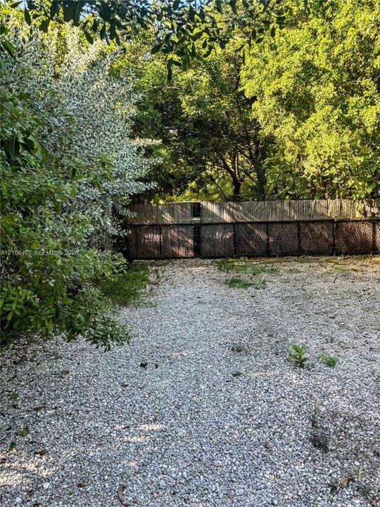 Gravel surface lot featuring a gated entrance, privacy fencing, and surrounding mature trees