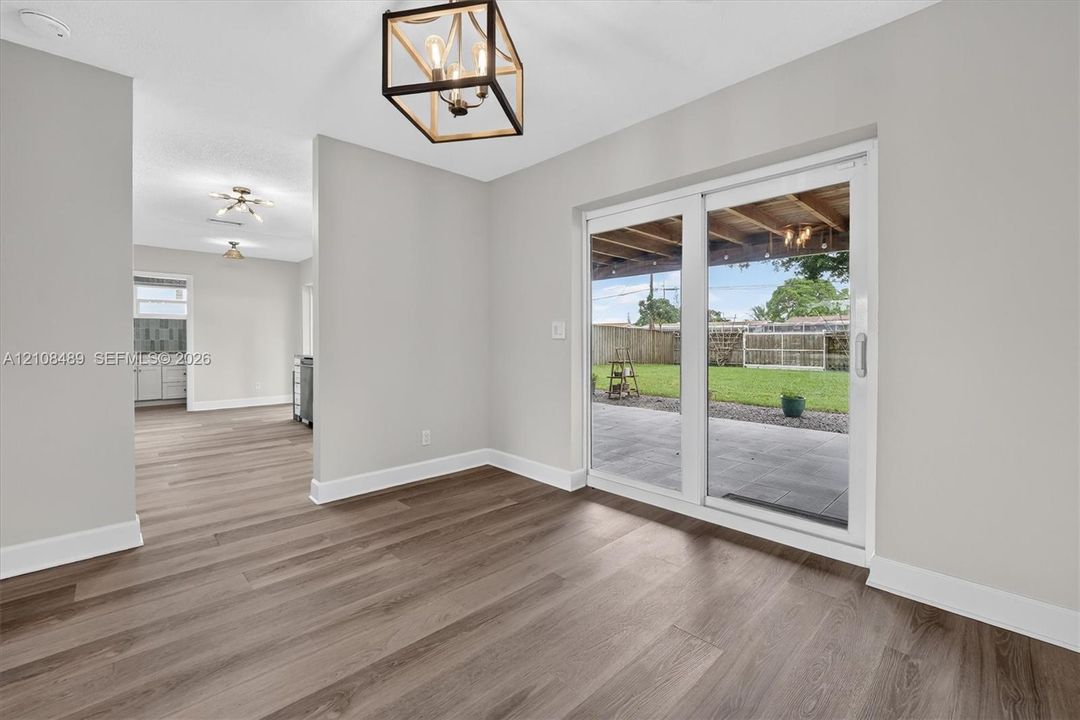 Wood-finish flooring, metal geometric chandelier, and sliding glass doors opening to a covered patio and fenced yard