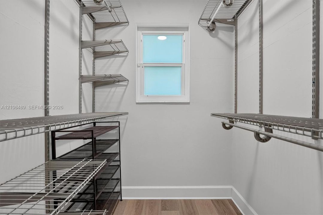Storage space featuring wall-mounted wire shelving, hanging rods, and wood-finish flooring with a single window