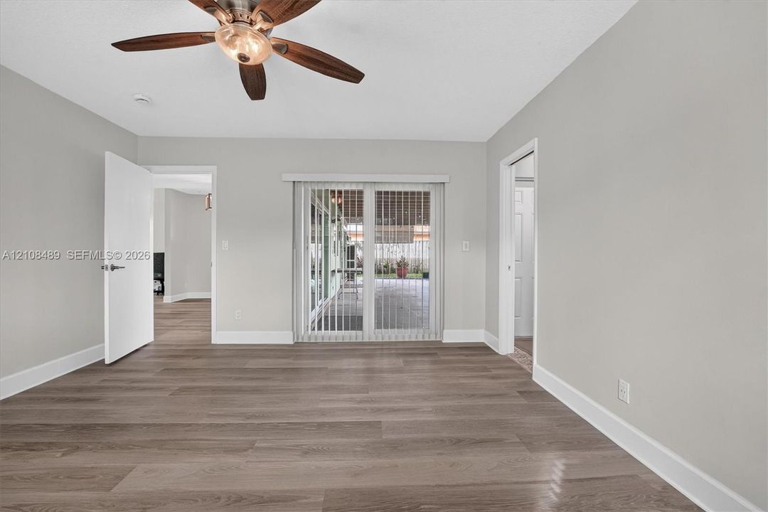 Room featuring wood-finish flooring, ceiling fan with light fixture, and sliding glass doors