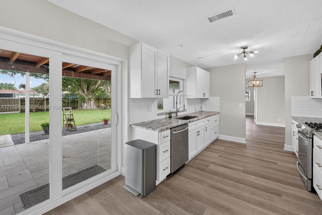 Kitchen featuring white cabinetry, stone-surface countertops, subway tile backsplash, stainless steel appliances, and sliding glass doors to a covered patio