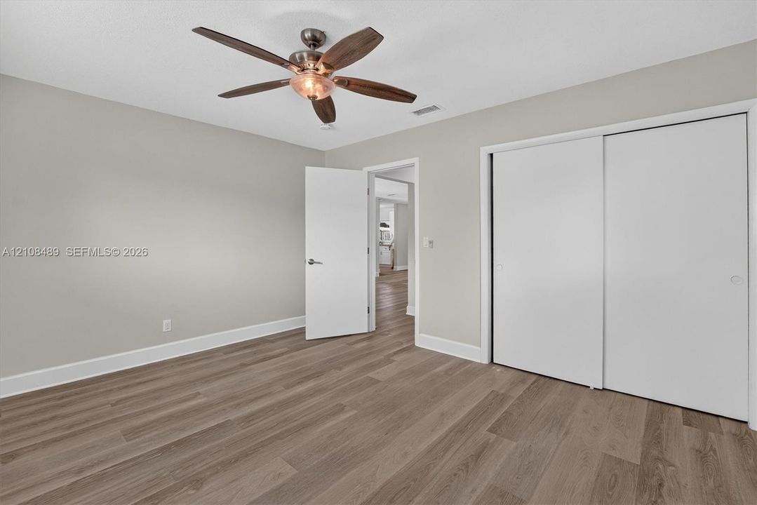 Wood-finish flooring, ceiling fan with integrated light fixture, and dual-panel sliding closet doors