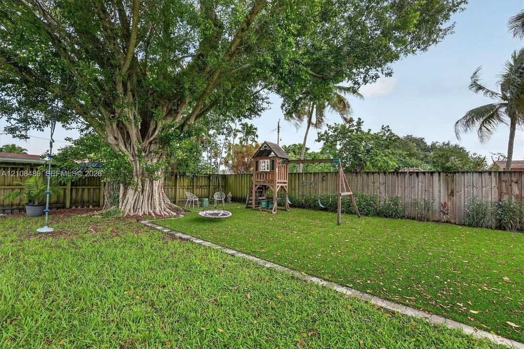 Backyard featuring synthetic turf, concrete paver edging, wood perimeter fencing, and a mature tree
