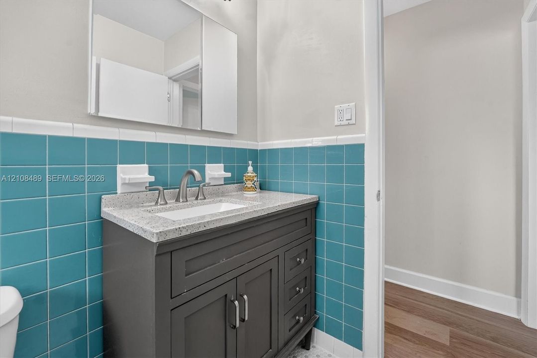 Vanity cabinet with shaker-style doors and drawers, speckled solid surface countertop, rectangular undermount sink, brushed nickel widespread faucet, and teal ceramic wall tiling