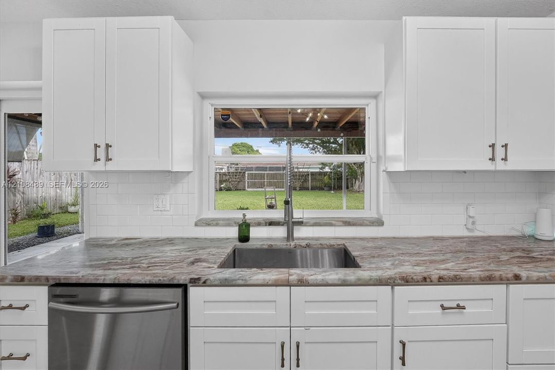 Kitchen featuring white shaker-style cabinetry, stone-patterned countertops, a stainless steel undermount sink with a gooseneck faucet, white subway tile backsplash, and a stainless steel dishwasher