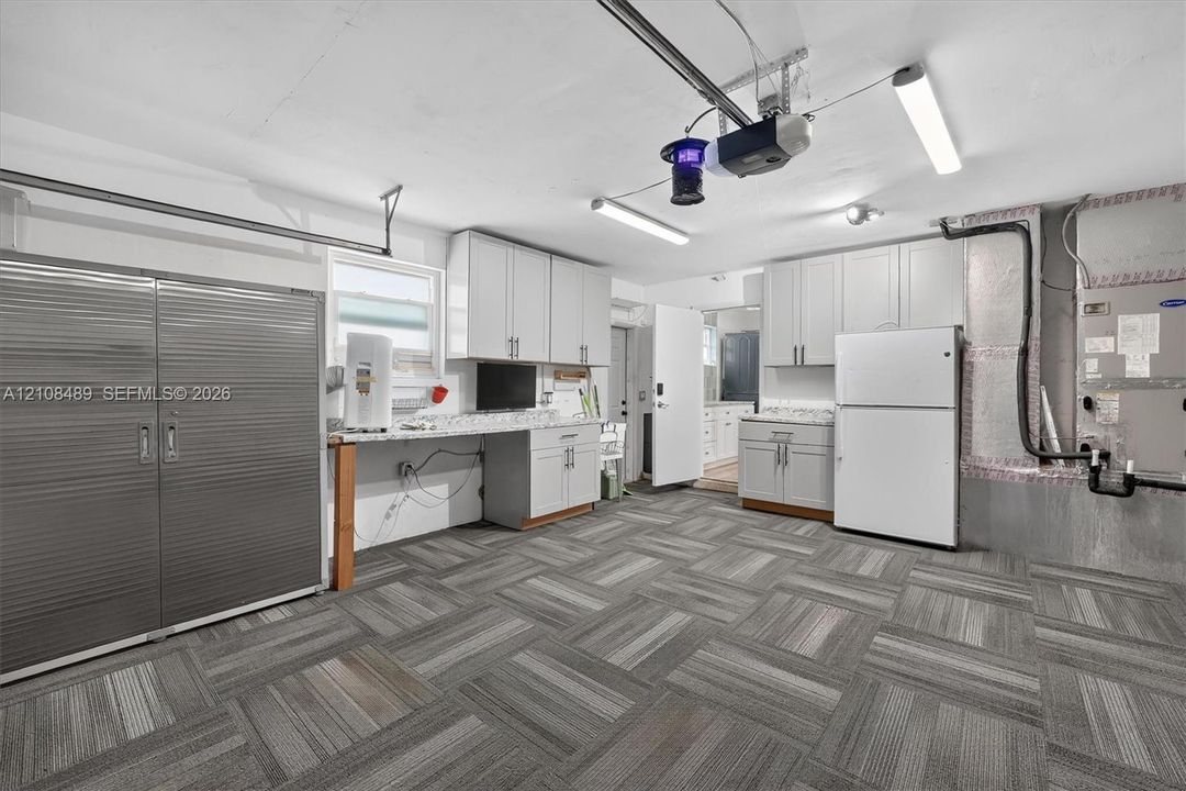Garage featuring modular carpet tile flooring, built-in light-grey cabinetry, light-colored countertops, and integrated linear lighting