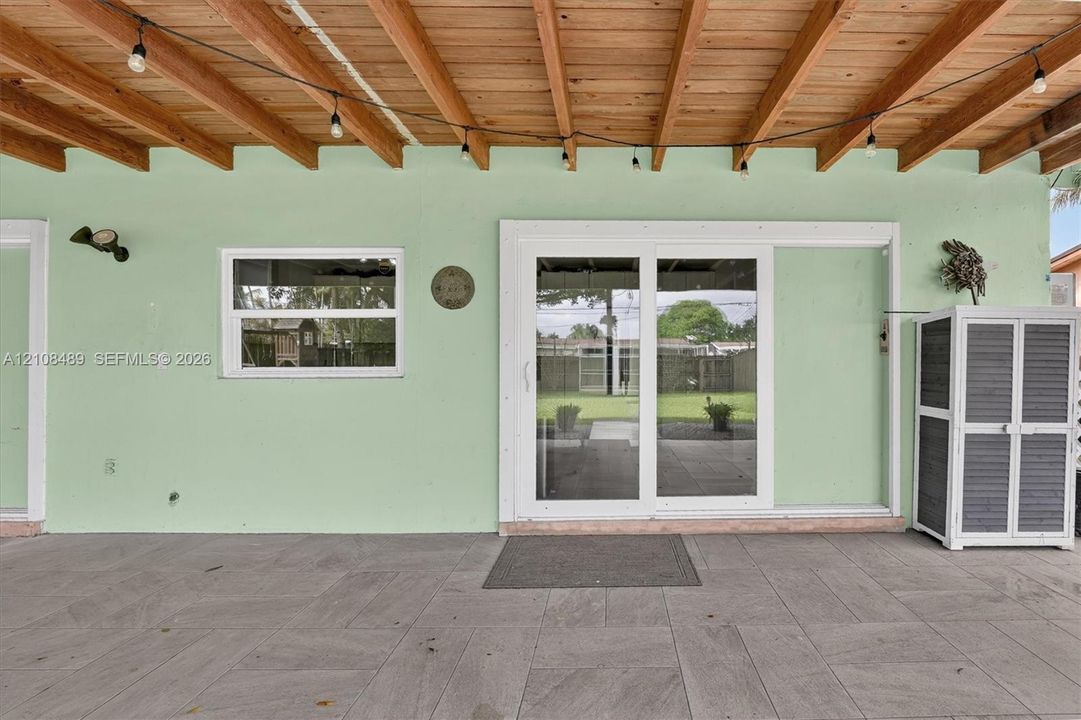 Covered patio featuring an exposed wood-beam ceiling, large-format tile flooring, and white-framed sliding glass doors