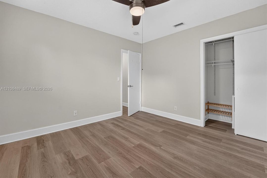 Neutral-toned interior space featuring wood-finish flooring, a ceiling fan with integrated lighting, and a closet with built-in wire shelving