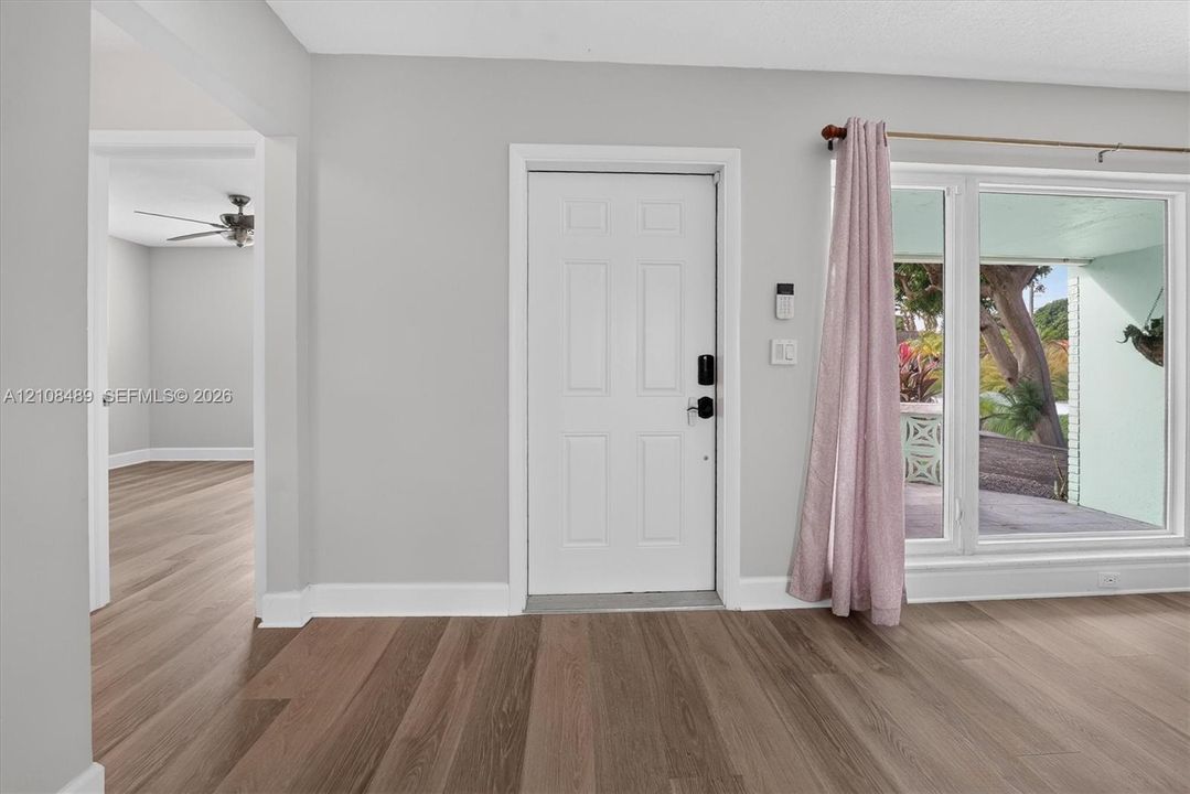 Neutral-toned interior featuring wood-finish flooring, a white six-panel entry door, and expansive glass window panes
