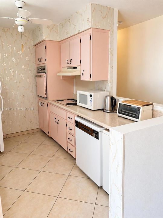 Kitchen featuring cabinetry with matte-finish hardware, solid-surface countertops, built-in wall oven, inset stovetop, and ceramic tile flooring