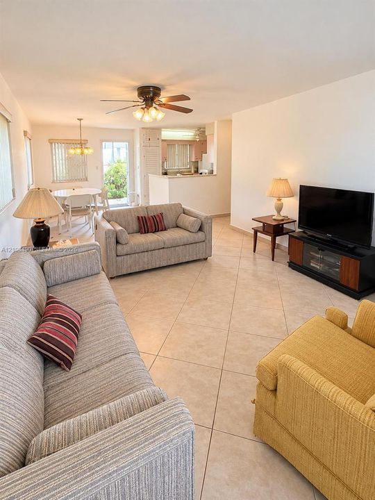 Open-concept interior featuring large-format ceramic tile flooring, a ceiling fan with integrated lighting, and a glass-paneled exterior door