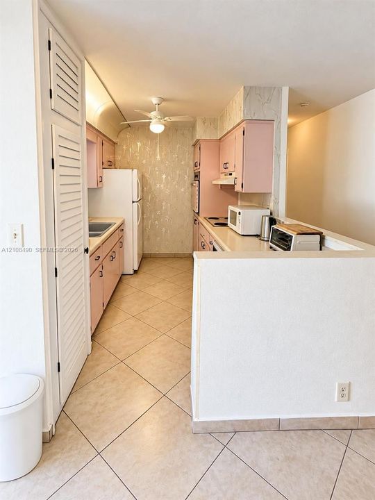Kitchen featuring cabinetry with integrated hardware, neutral tile flooring, built-in pantry with louvered doors, and a ceiling-mounted light fixture with fan