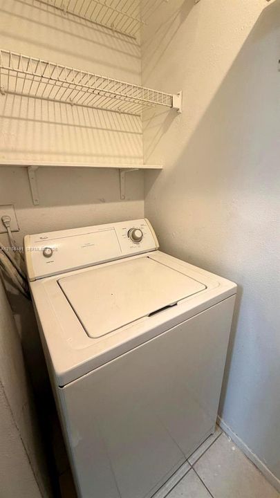 Dedicated laundry area featuring a top-load washer, installed wire shelving, and tiled flooring