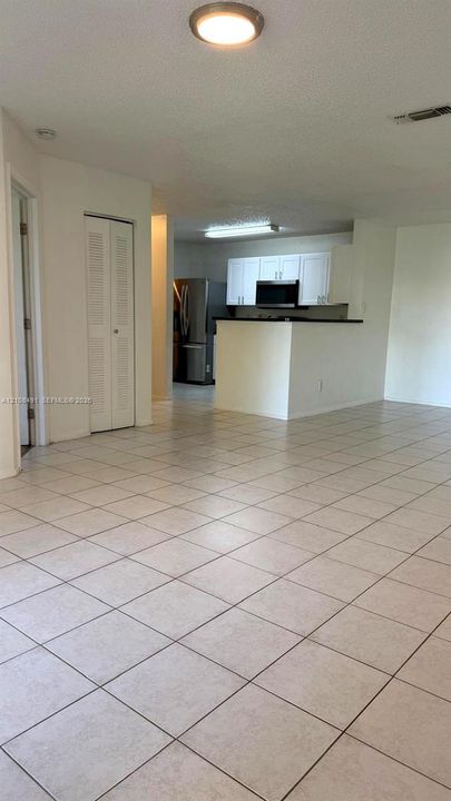 Open-concept interior featuring neutral tile flooring, white cabinetry, integrated stainless steel appliances, and a breakfast bar
