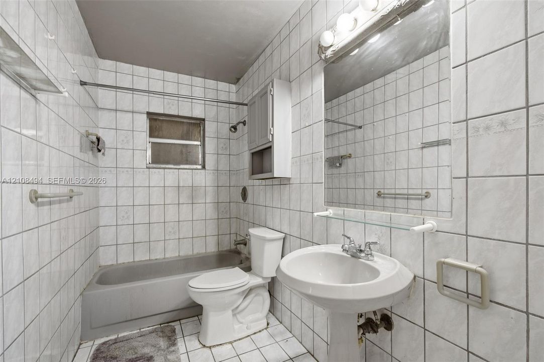 Full-height tile wall surround, white pedestal sink, integrated wall-mounted medicine cabinet, wall-to-wall mirror with glass shelving, and porcelain tub with shower head fixture