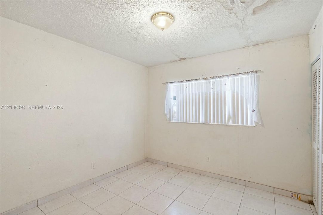 Room featuring white tile flooring, ceiling-mounted flush lighting, and a louvered bi-fold closet door