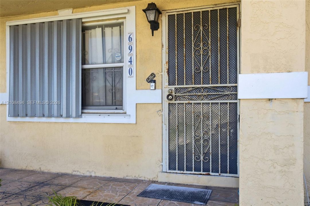 Stucco exterior entry featuring a decorative metal screen door, exterior storm shutters, and tiled porch flooring