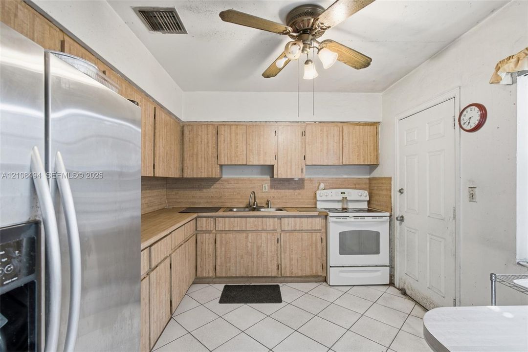 Kitchen featuring wood-finish cabinetry, stainless steel refrigerator, white free-standing range, double-basin sink, and tile flooring