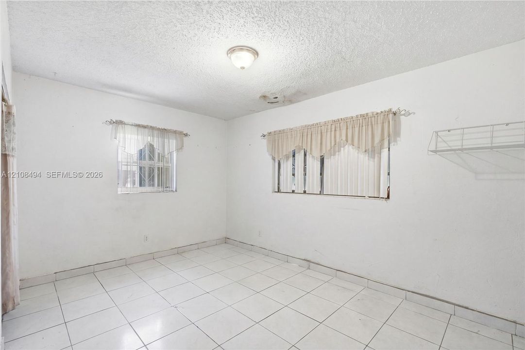 Interior space featuring white floor tiles, a dual-window configuration, a flush-mount ceiling light fixture, and a built-in wire wall shelf