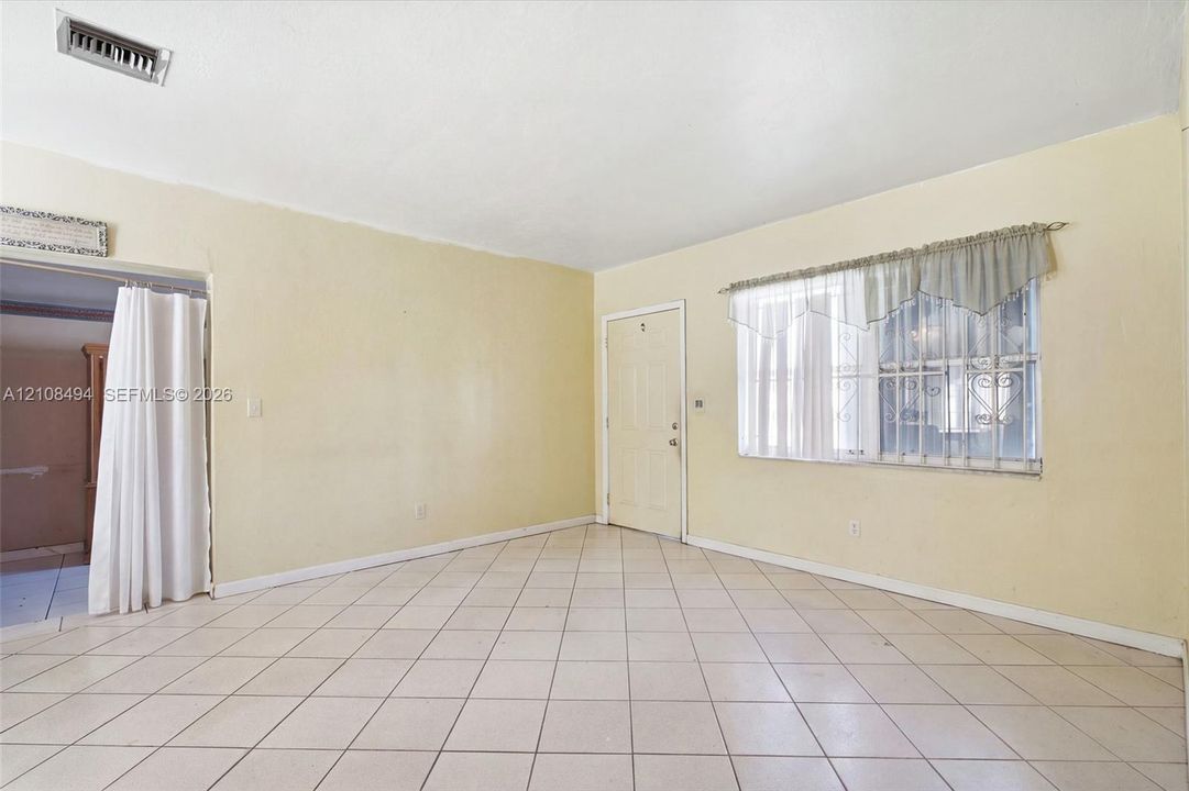 Interior space featuring diagonal-patterned ceramic tile flooring, neutral wall paint, and a window equipped with metal security bars