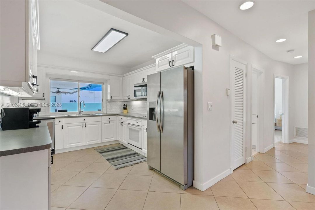 Kitchen featuring white cabinetry, stainless steel side-by-side refrigerator, built-in microwave, tile flooring, and recessed lighting