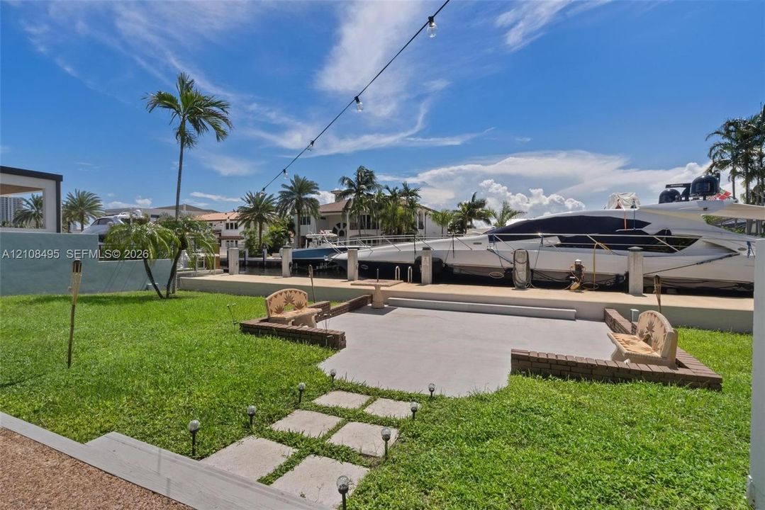 Waterfront backyard featuring a concrete patio, stone-surfaced retaining walls, manicured lawn, and a private bulkhead boat dock