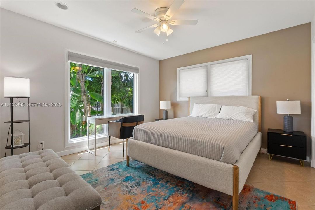 Spacious room featuring neutral wall tones, large windows, tile flooring, and a ceiling fan with integrated lighting