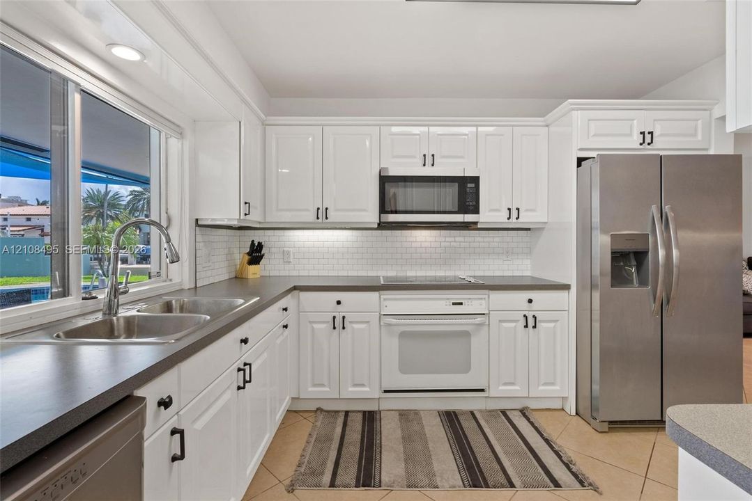 Kitchen featuring white cabinetry, subway tile backsplash, dark solid-surface countertops, stainless steel side-by-side refrigerator, and double-basin sink with pull-down faucet